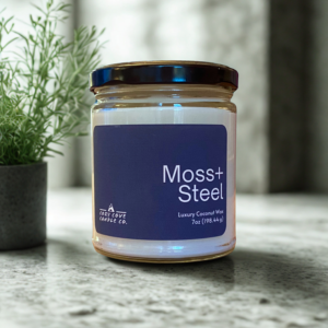 moss and steel candle sitting on a marble countertop in front of a plant