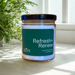 refresh and renew candle sitting in front of a window with green plants